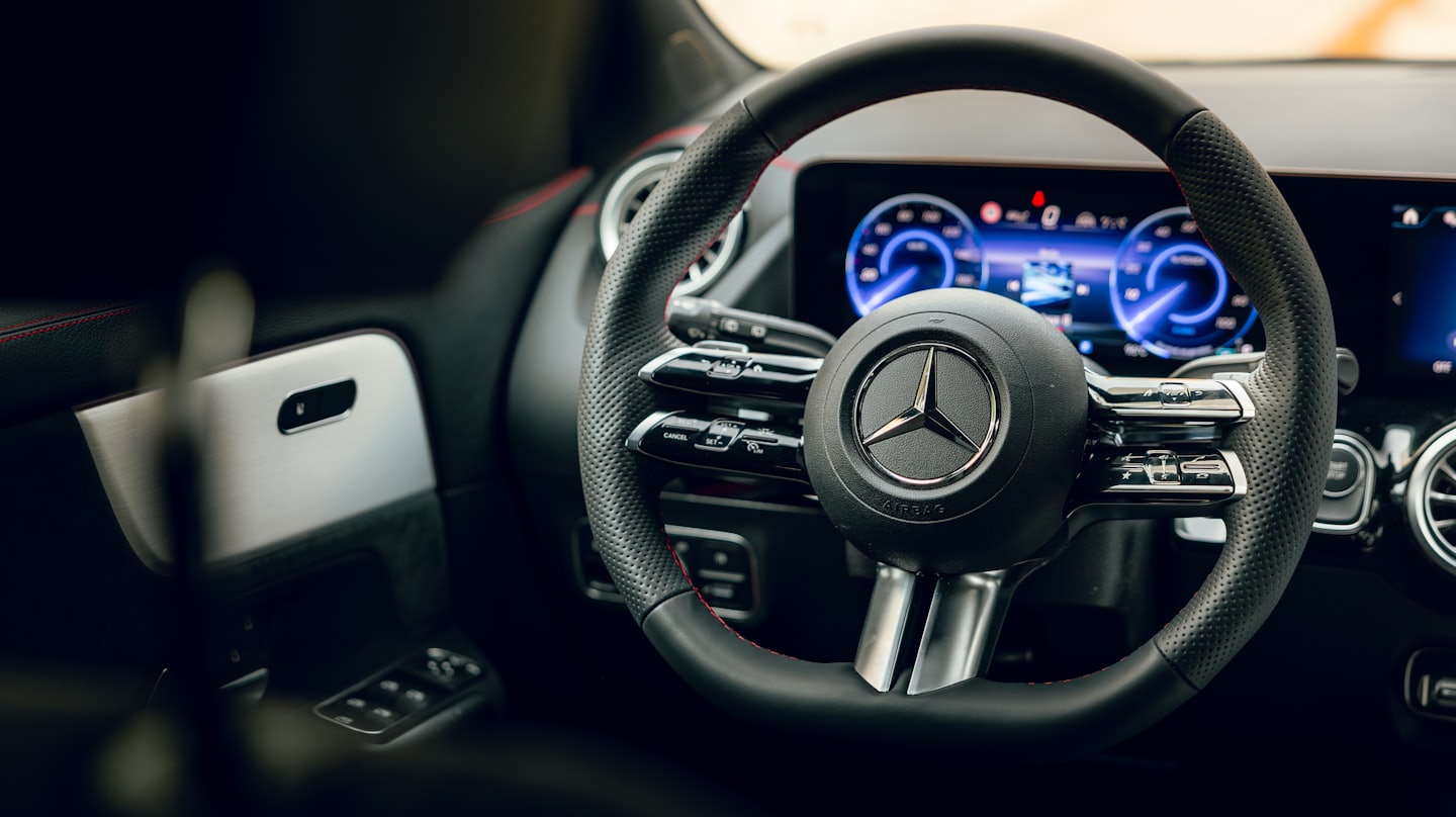 Black leather steering wheel with red stitching inside a car.